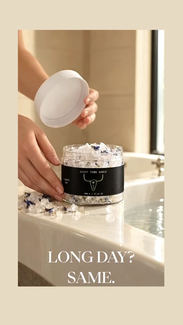 A hand opening a jar of The Soak bath salts at the edge of a bath